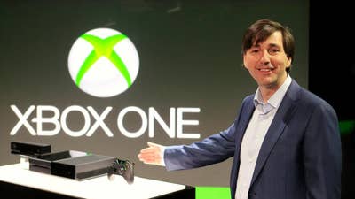 Don Mattrick gestures at an Xbox One on a pedestal like a game show model highlighting a prize